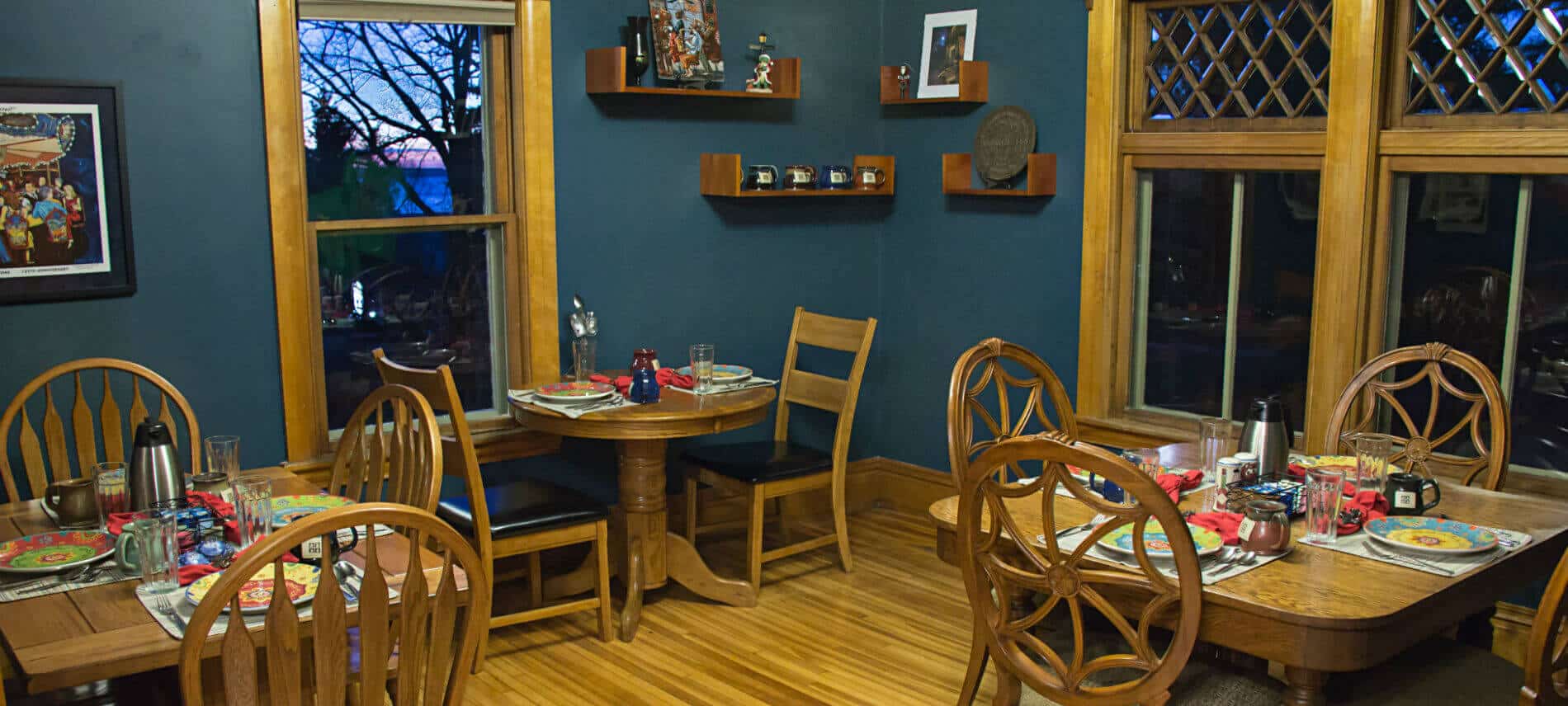 Blue dining room with wood floors, three individual dining tables set for breakfast, and large windows
