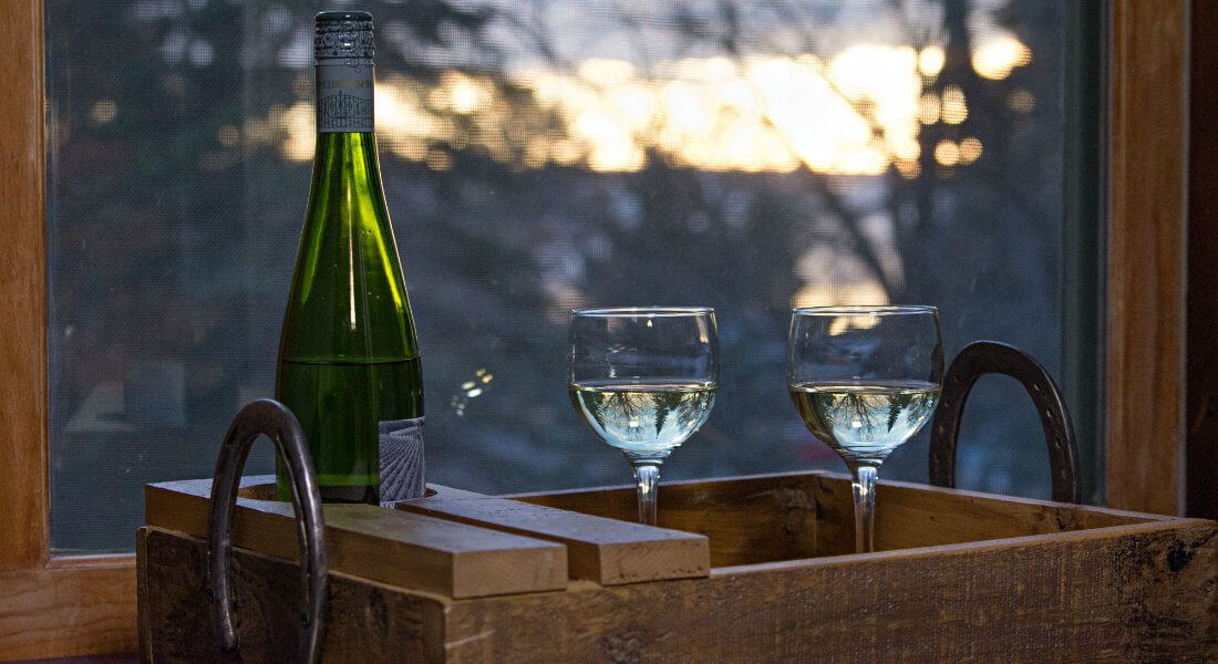 Wood tray topped with a wine bottle and two glasses in front of a window