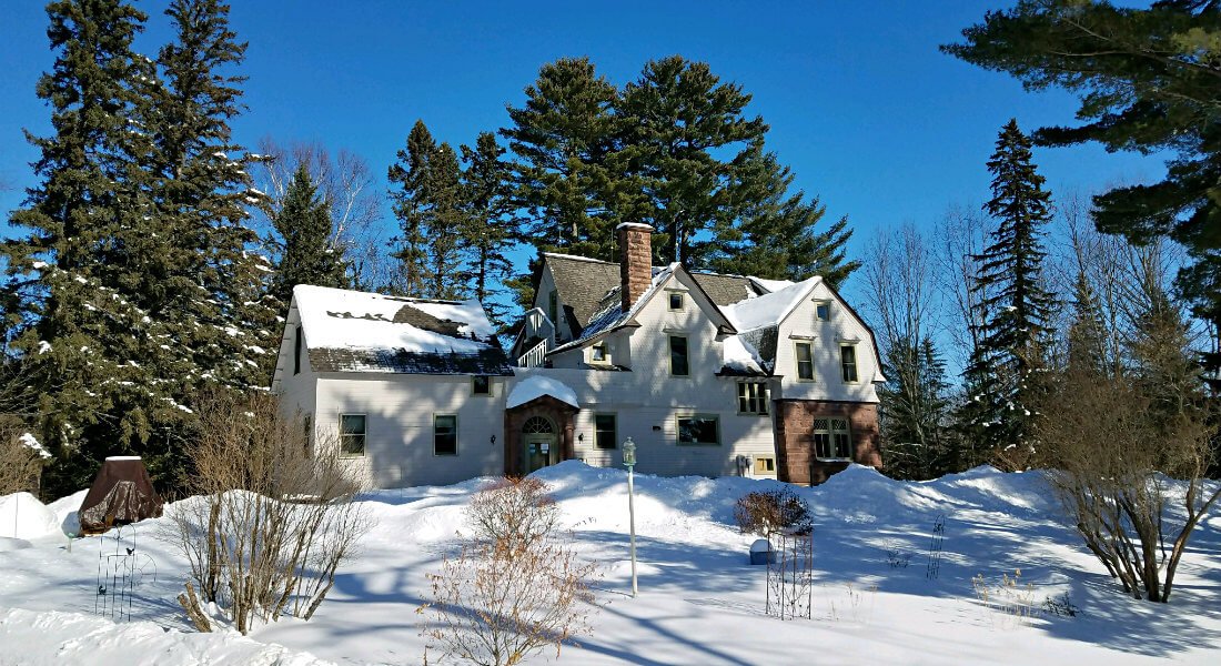 Snow covered lawn with green pines, and the inn in the backround amidst crisp blue skies