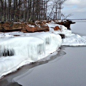 sandstone shoreline covered with ice, winter trees above caves and icy waters