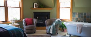 guest room with green walls, corner fireplace, large clawfoot tub and two gray upholstered chairs