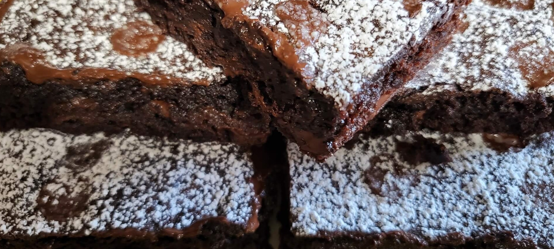 Stack of dark chocolate brownies with chocolate chips, sprinkled with powdered sugar.