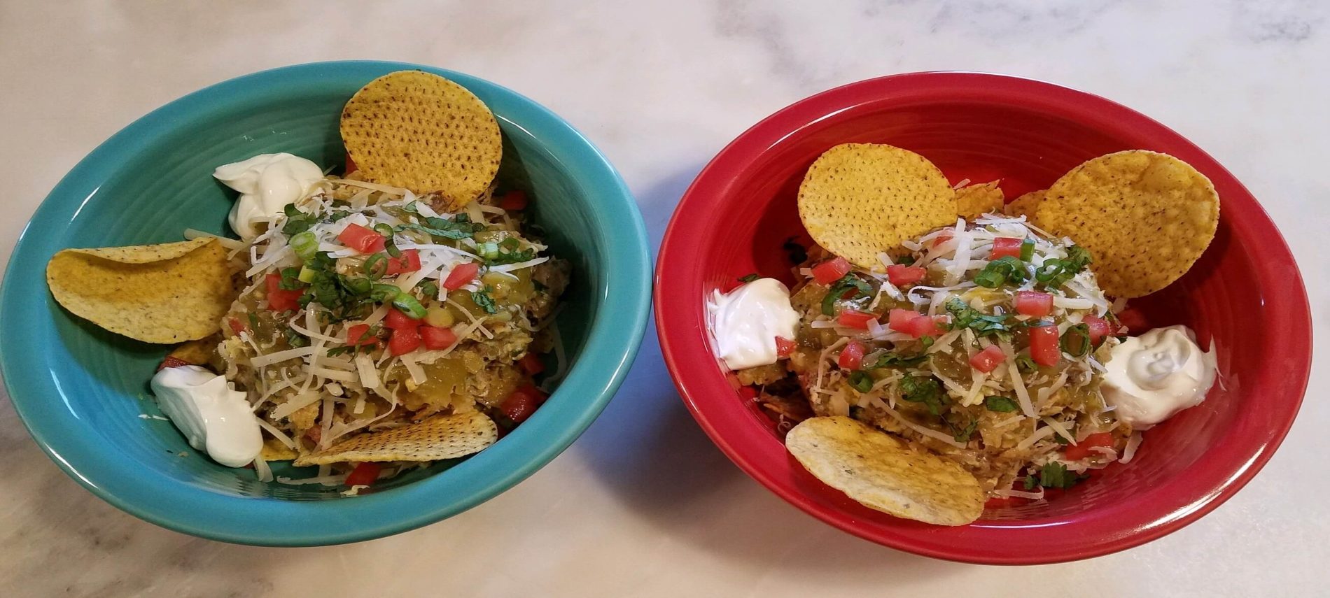 red and turquoise bowls with egg and pork mixture in center with tortilla chips, sour cream, dice tomatoes and green onions
