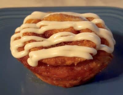 light brown muffin with cinnamon swirl, topped with cream cheese glaze on blue plate