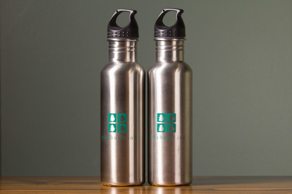 Two stainless steel water bottles with pinehurst inn logo on wood table and green background