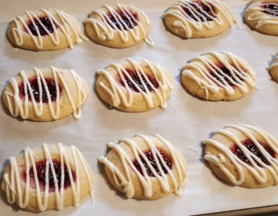butter cookies with raspberry jam and white chocolate drizzle on parchment paper