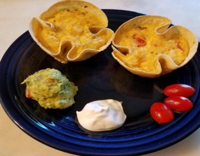 Two small quiches in a corn tortilla on a cobalt blue plate with a scoop of guacamole and sour cream