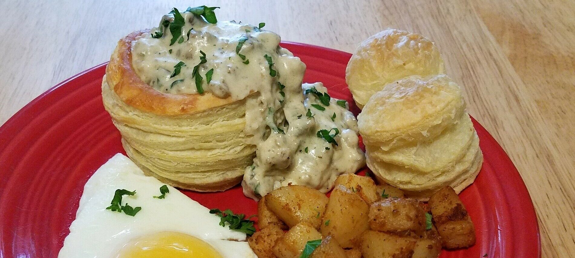red plate with a golden-brown puff pastry bowl filled with a sausage and mushroom gravy with seasoned diced potatoes and sunny side up egg