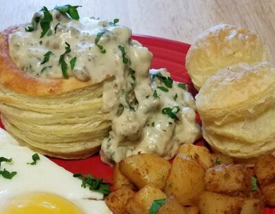 red plate with a golden-brown puff pastry bowl filled with a sausage and mushroom gravy with seasoned diced potatoes and sunny side up egg