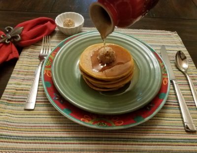 sweet potato pancakes with pecan butter on green plate with syrup being poured on pancakes