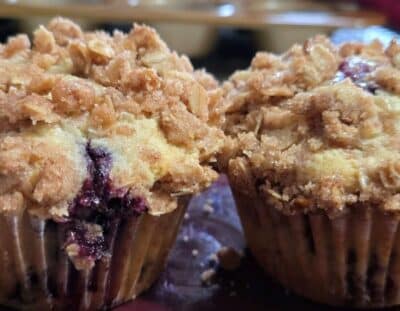 Two homemade blueberry muffins with crumble on top on a maroon plate