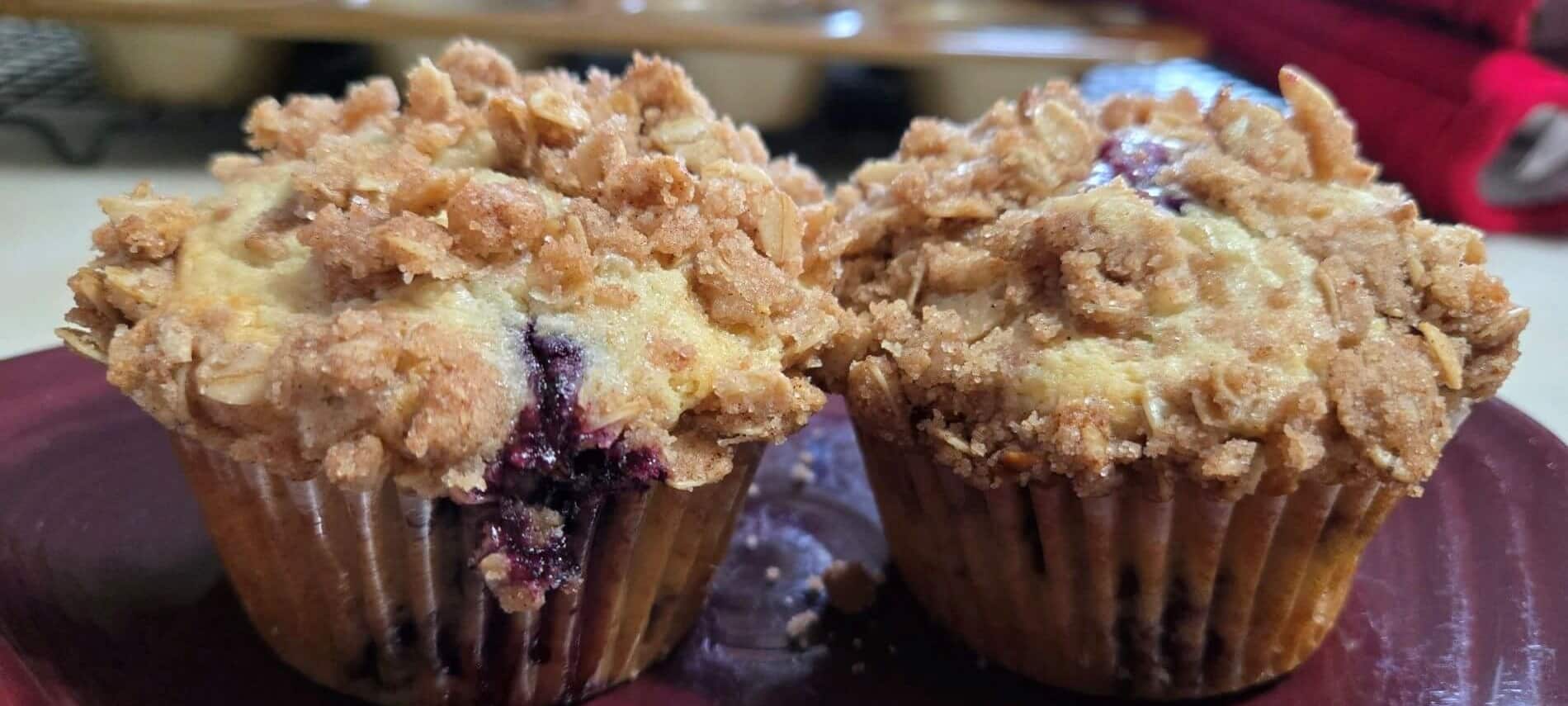 Two homemade blueberry muffins with crumble on top on a maroon plate