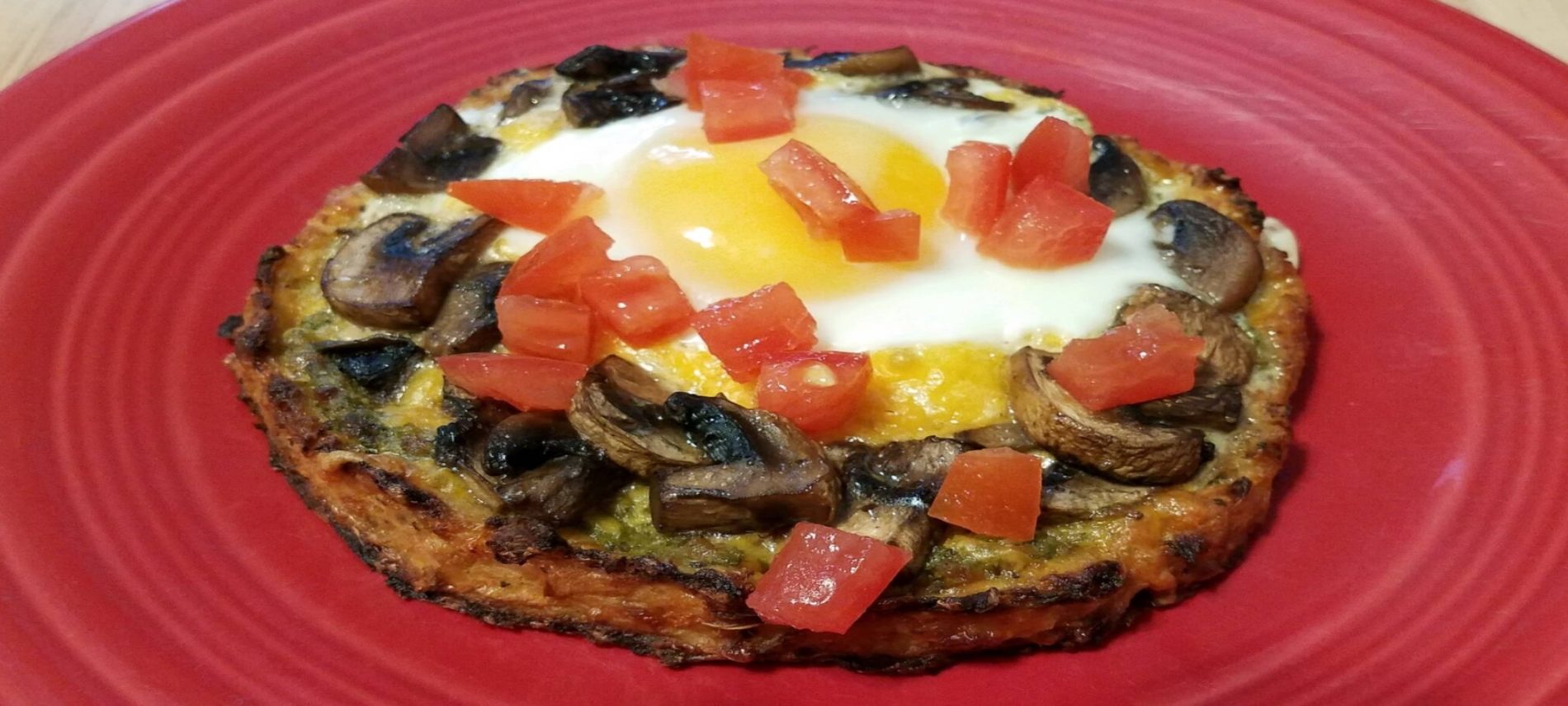 small round pizza with mushrooms, egg and yellow yolk topped with chopped tomatoes on a red plate