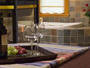 Tray of red and green grapes, two wine glasses and a bottle of wine with soaker tub in the background