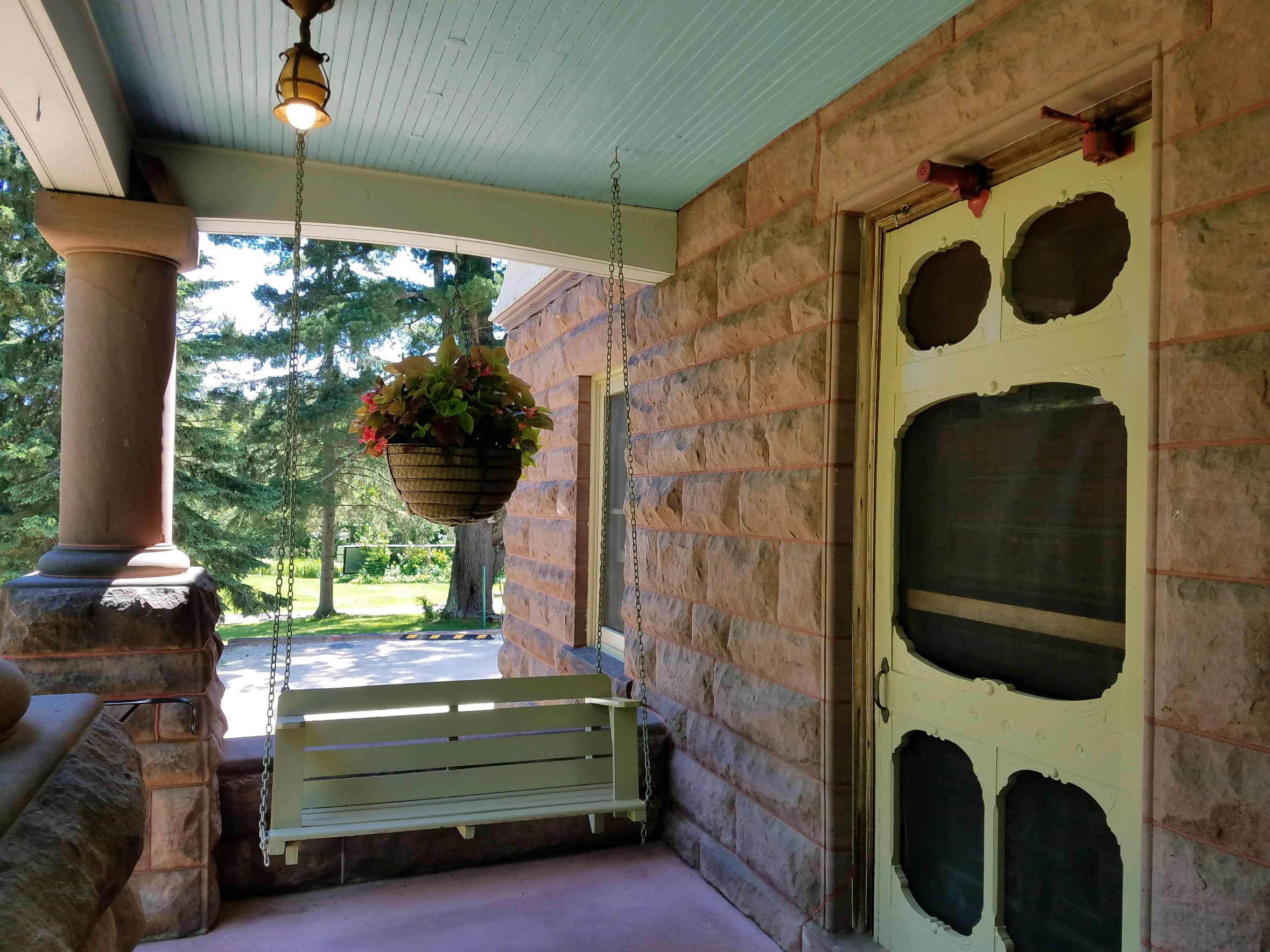 brownston front porch with green antique screen door, porch swing and hanging basket