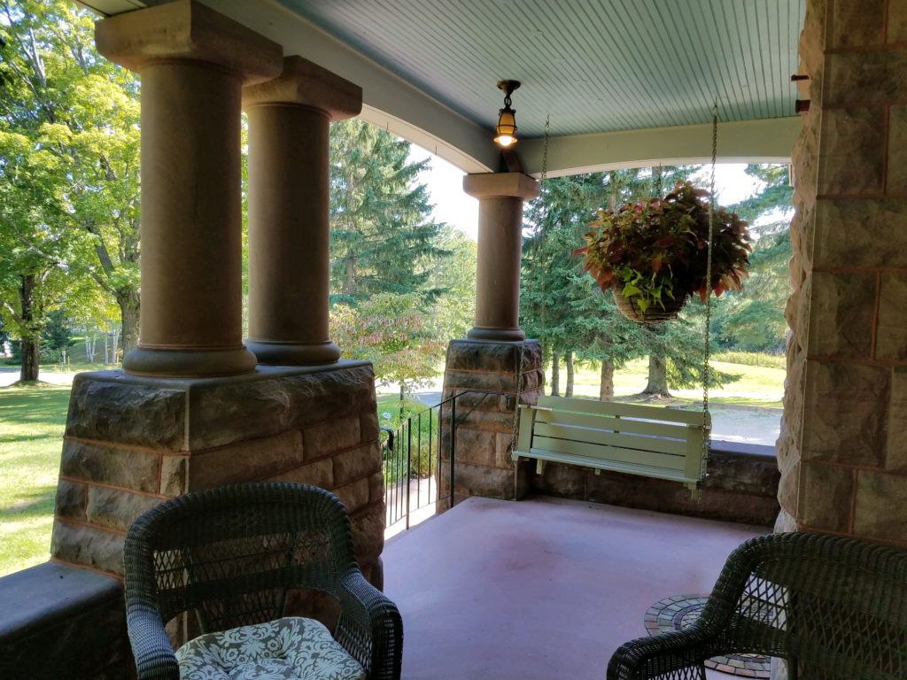 porch with brownstone colums, porch swing, wicker seating with cream cushion and hanging plant