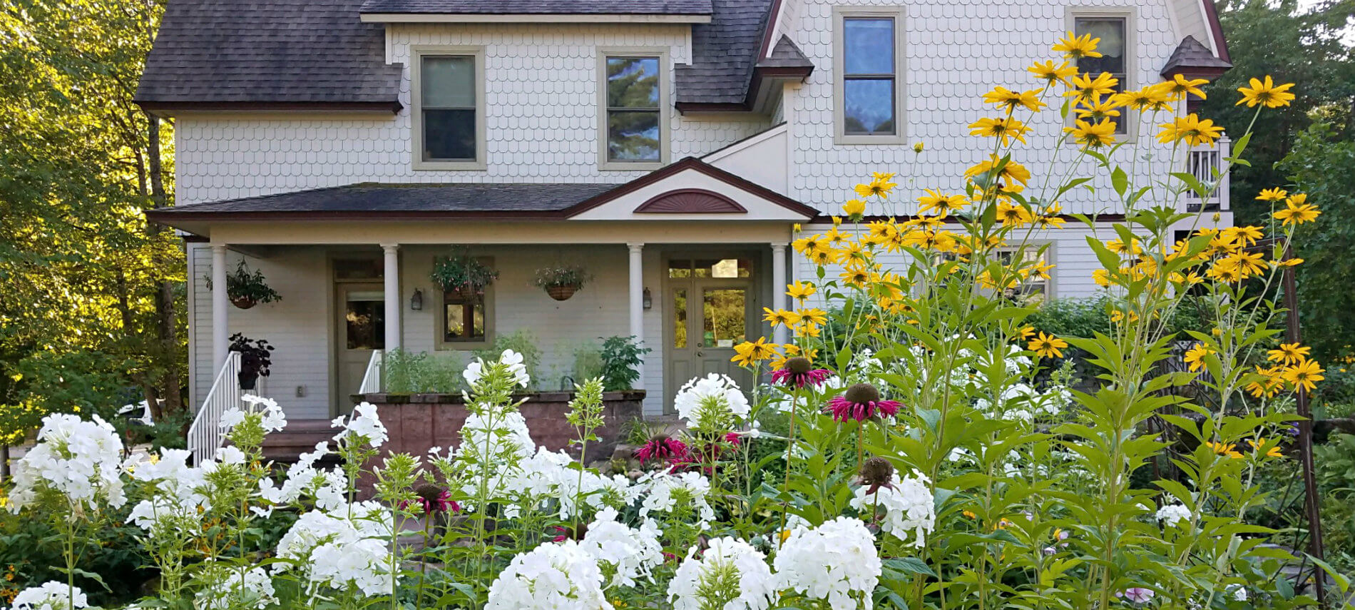 Exterior view of the inn with covered porch surrounded by lush green grass, trees and colorful flowers