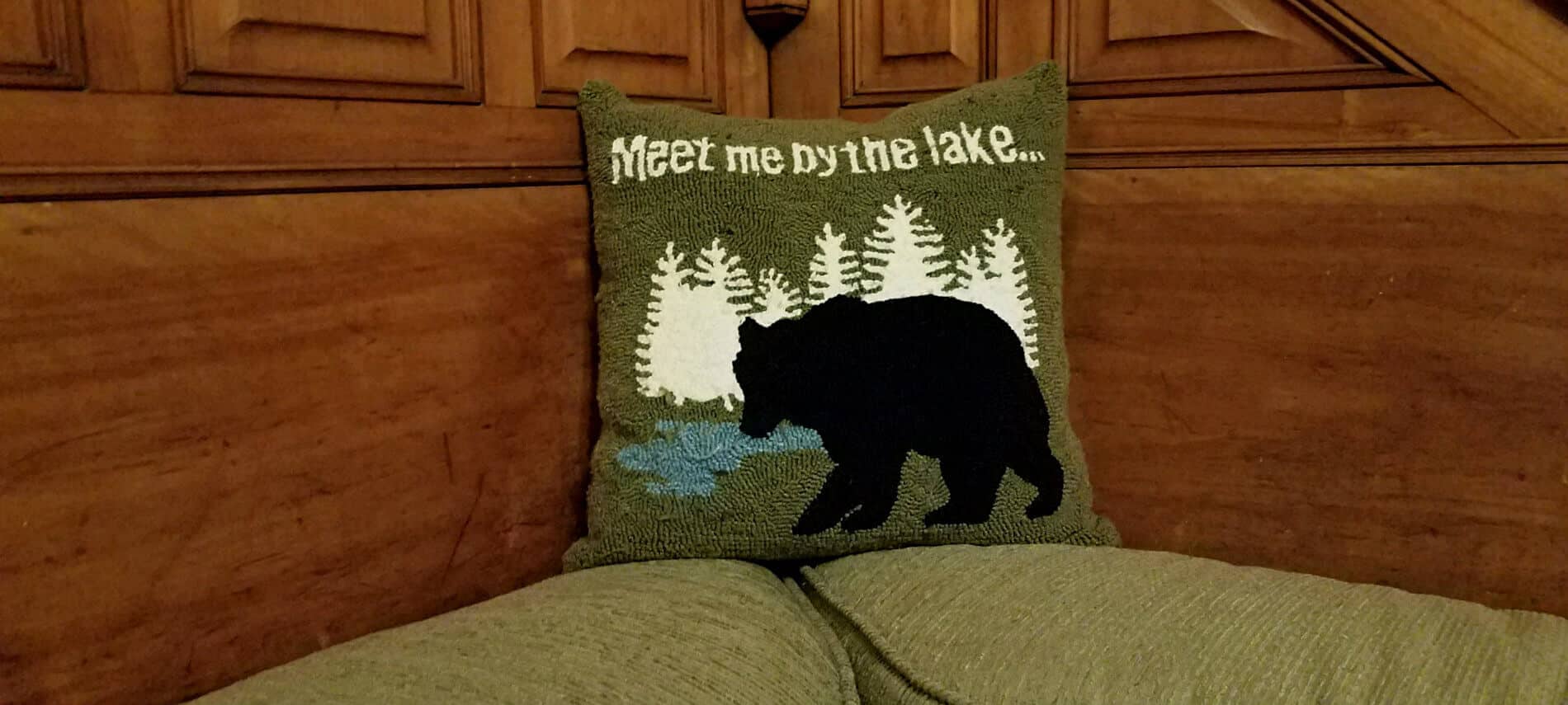 Close up view of green throw pillow that says, Meet me by the lake...