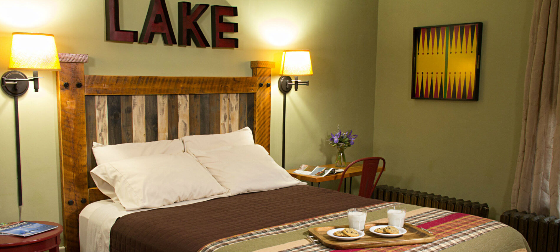 Light green guest room, bed with wood headboard and tray of cookies and milk, nightstands and reading lights