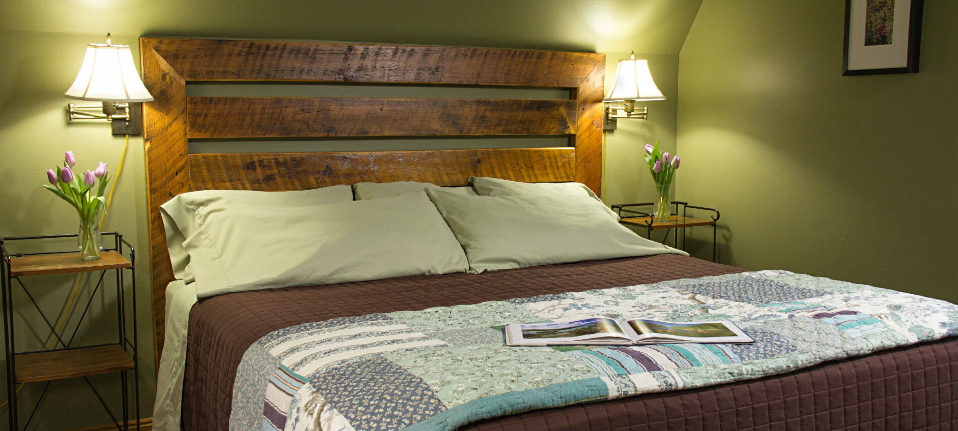 Green guest room with sloped ceilings, wood slatted bed with flanking nightstands and reading lights
