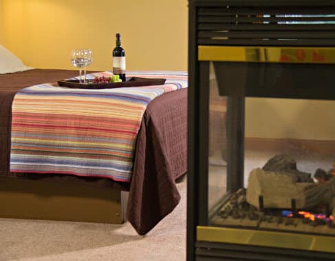 Golden painted guest room with carpet, bed topped with tray of grapes and wine, and a fireplace