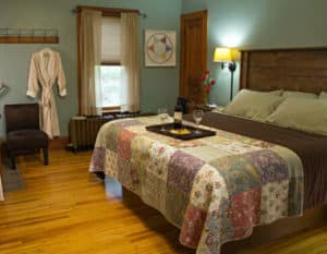 Blue green guest room with wood floors, wood headboard with quilt covering topped with tray of grapes and wine