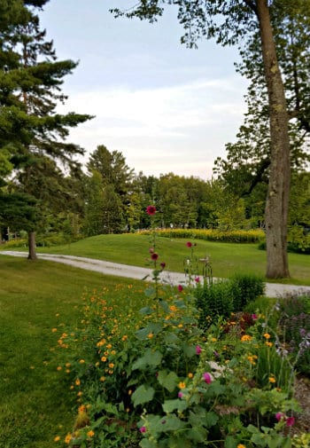 Rolling grassy lawn surrounded by trees with colorful flowers in the foreground