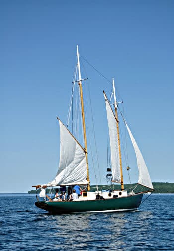 Green sailboat with white sails in the open water amidst blue skies